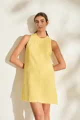 Vestido corto de lino italiano, sin mangas, con cuello redondo y detalles de terminaciones desflecadas en el escote, costura central y dobladillo.