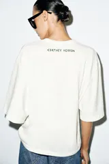 Camiseta rústica de color blanco, de corte regular, con cuello redondo, mangas por debajo del codo y diseño estampado a contraste en el centro del frente.