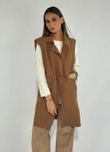 Chaleco largo color marrón, con solapas, un botón frontal y bolsillos laterales. Presenta costuras decorativas en contraste.