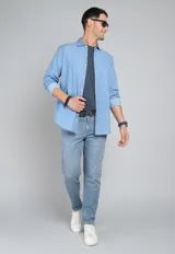 Camisa de jean azul con botones blancos, mangas largas con puños doblados y corte clásico.