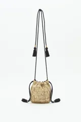 Cartera tipo saco de tamaño pequeño, confeccionada con tejido brillante en color dorado. Presenta cierre mediante cordones ajustables con borlas negras en los extremos y una correa larga de hombro con detalles decorativos y borlas adicionales.