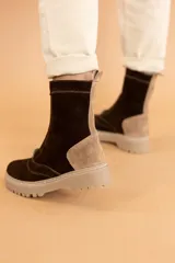 Bota tipo borcego de caña media, confeccionada en una combinación de cuero gamuzado negro y detalles en cuero color suela en la parte trasera y lengüeta. Presenta suela track de goma negra y costuras a la vista.