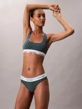 Bralette deportivo sin relleno ni forro, con diseño de espalda cruzada y banda elástica inferior con el logo de la marca. Presenta un estampado geométrico con el monograma de Calvin Klein en tonos verde oscuro y negro.