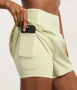 Bermuda deportiva de microfibra color azul petróleo, con diseño de doble capa que incluye un short interno ajustado y una capa externa suelta. Presenta cintura alta, bajo redondeado y bolsillo funcional en el short interno.