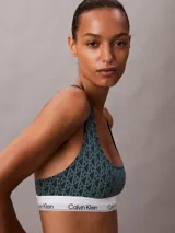 Bralette deportivo sin relleno ni forro, con diseño de espalda cruzada y banda elástica inferior con el logo de la marca. Presenta un estampado geométrico con el monograma de Calvin Klein en tonos verde oscuro y negro.