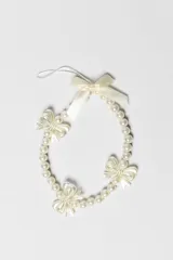 Correa para celular de cuentas de perlas blancas con detalles de lazos decorativos.