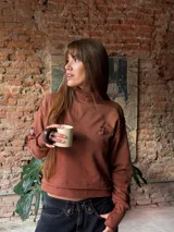 Buzo de algodón rústico con cuello polera, corte boxy y costuras externas visibles. Presenta puños con abertura para el pulgar y un pequeño bordado en el pecho.