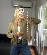 Cárdigan de tejido de punto color crema, con cuello redondo, mangas largas y cierre frontal con botones metálicos. Presenta detalles de flecos en los puños y en el ruedo.