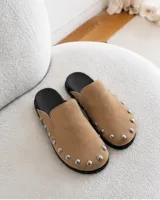 Zuecos de ante color beige con diseño destalonado, punta redonda y tachas metálicas plateadas alrededor de la suela.