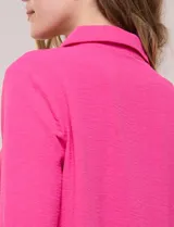 Blusa verde de calce holgado y caída fluida, confeccionada en tejido tipo crepé. Cuenta con cuello camisero con solapa, escote en V y cierre parcial al frente con tres botones metálicos. Las mangas son largas con puños abotonados.
