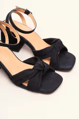 Sandalia de gamuza color beige con taco cuadrado, tira ajustable con hebilla en el tobillo y detalle de nudo en la tira delantera.