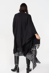 Ruana de tejido suave y envolvente en color blanco, con diseño de corte amplio y terminación de flecos en el ruedo.