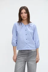 Camisa de manga larga con diseño a rayas celestes y blancas, cuello redondo y cartera de botones frontales. Presenta mangas con puños elásticos.