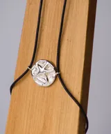 Pulsera con cordón negro y dije redondo plateado con diseño de estrella de mar.