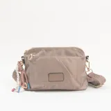 Bandolera de nylon color beige con cierre principal y bolsillo frontal. Incluye correa ajustable con diseño tejido y detalle de colgantes decorativos en uno de los laterales.