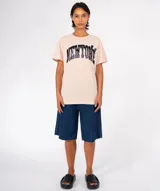 Remera de manga corta color beige claro con cuello redondo. Estampado frontal con la palabra "NEWTONE" en tipografía universitaria, con relleno oscuro y detalles de apliques circulares negros.