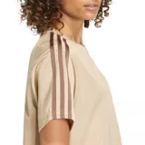 Remera Adidas Firebird color beige, con cuello redondo, mangas cortas y las tres rayas características de la marca en color marrón en los hombros. Incluye el logo del trébol de Adidas bordado en el pecho.