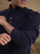 Sweater de punto en color beige, con cuello alto y cierre frontal parcial de botones. Presenta mangas largas con puños acanalados y diseño de corte clásico.