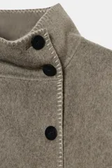 Cazadora de corte amplio confeccionada en hilatura con lana, color beige. Presenta cuello subido, manga larga y cierre frontal con botones negros. Destaca por sus acabados con costuras de hilo a contraste en los bordes.