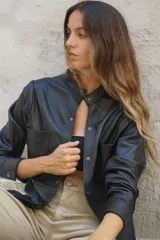 Camisa negra de cuero ovino con cuello mao, cierre frontal con botones a presión, dos bolsillos de parche en el pecho y tachas doradas en cuello, bolsillos y mangas.