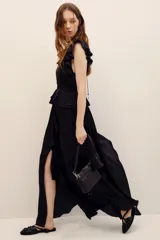 Vestido largo negro de poliéster, con escote en V profundo, mangas sisa con volados en los hombros, cintura elastizada con diseño fruncido y falda larga con capas y volados.