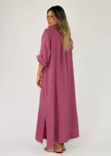 Vestido largo de lino color tostado, con diseño camisero, botonadura frontal completa con detalles de volados a lo largo de la botonadura, mangas largas arremangables y aberturas laterales en el bajo.