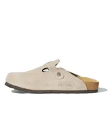 Zuecos de cuero gamuzado natural en color beige, con diseño de punta cerrada y talón descubierto. Presentan una plantilla anatómica de corcho y látex, con detalle de hebilla metálica grabada con el logo de la marca y nombre de la marca grabado en el lateral.