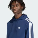 Canguro Adidas Originals de color azul, con capucha ajustable mediante cordones, bolsillo frontal tipo canguro y las icónicas tres rayas blancas en las mangas. Presenta el logo del trébol bordado en el pecho.