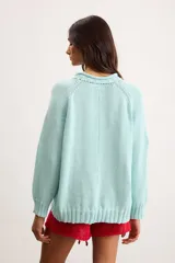 Sweater de punto color marfil con diseño de velero en la parte frontal, cuello con capucha y cordón rojo de ajuste.