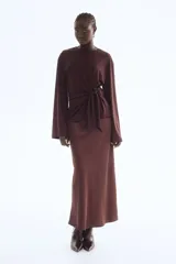 Top de manga larga color bordó, confeccionado en punto suave, con escote redondo y hombros caídos. Presenta un detalle de nudo y tiras laterales en la cintura.