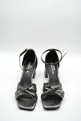 Sandalia de tacón medio ancho con diseño de nudo frontal y pulsera ajustable al tobillo con hebilla metálica.