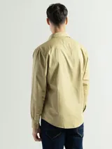 Camisa de manga larga confeccionada en tela canvas de algodón, color beige. Presenta cuello clásico, cierre frontal con botones y dos bolsillos frontales con tapa.