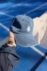 Gorra tipo baseball de color azul con efecto lavado, con bordado frontal de un escudo con una piña en el centro.
