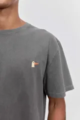 Remera de algodón color marrón con efecto lavado, de corte clásico y cuello redondo. Presenta un pequeño bordado de un pájaro en el pecho.