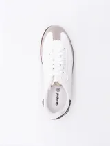 Zapatilla estilo urbano de color blanco, con refuerzo de gamuza gris en la puntera, suela de goma marrón y detalles en negro en el talón.