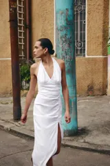 Vestido midi de lino con cuello halter y escote en pico. Presenta un diseño con frunces en el delantero, abertura lateral y cierre posterior con cremallera oculta y botones.