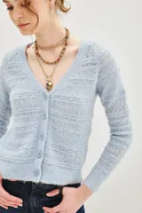 Cardigan de punto calado en color beige, con escote en V y cierre frontal de botones. Presenta un diseño de textura con franjas horizontales y mangas largas.