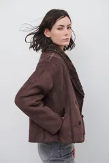 Chaqueta tipo gamulán de color marrón, con solapas amplias forradas en corderito sintético oscuro. Presenta un diseño cruzado con botones frontales y mangas largas, ideal para un estilo invernal.