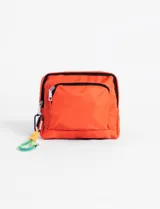Bolso bandolera de tela color naranja, con cierre frontal y compartimento principal con cierre. Incluye un mosquetón metálico con un llavero de cuerda trenzada multicolor.