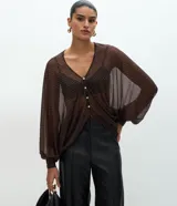 Blusa de poliamida con estampado geométrico, diseño amplio y fluido, escote en V con cierre frontal de botones, mangas largas abullonadas con puños ajustados y acabado con sutil transparencia.