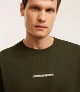 Remera verde militar de algodón, corte clásico, con cuello redondo y mangas cortas. Estampado frontal con texto en color claro.