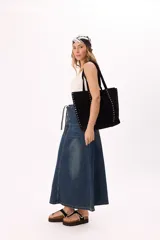 Bolso tipo tote de gamuza sintética en color marrón, con diseño amplio y manijas largas. Presenta dos líneas verticales de tachas metálicas plateadas en el frente y en los laterales.