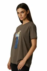 Remera de algodón color marrón topo, de corte al cuerpo y cuello a la base. Presenta un estampado frontal con diseño artístico de una figura humana con detalles en glitter.