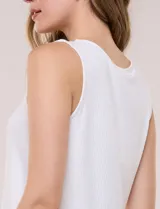 Musculosa blanca de tejido acanalado, con escote redondo adornado con tachas metálicas en el borde y breteles anchos.