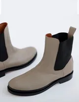 Bota Chelsea color hueso de cuero vacuno, con elástico lateral negro y suela de cuero.