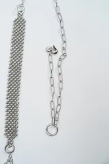 Cinturón de cadena plateada con diseño de malla central de esferas pequeñas y terminaciones con dijes en forma de corazón.