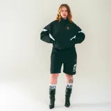 Campera deportiva negra de nylon liviano con paneles diagonales blancos en contraste. Presenta un estampado frontal discreto y un gran gráfico en la espalda que incluye una silla naranja con un gato blanco durmiendo y la frase "Sin siesta no hay fiesta".