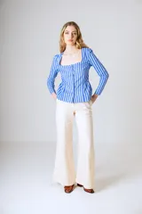 Blusa de manga larga con estampado de rayas verticales en tonos azul y blanco. Presenta un escote cuadrado, cierre frontal con botones y un diseño con corte peplum en la cintura.