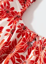 Vestido corto de algodón con estampado de margaritas rojas sobre fondo blanco. Presenta un diseño evasé, escote cuadrado con cierre de lazo ajustable, mangas cortas abullonadas y forro interior.