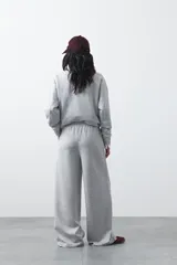 Pantalón de corte holgado y pierna ancha, con cintura elástica ajustable mediante cordón. Presenta bolsillos laterales y costuras verticales decorativas que recorren el frente de las piernas.